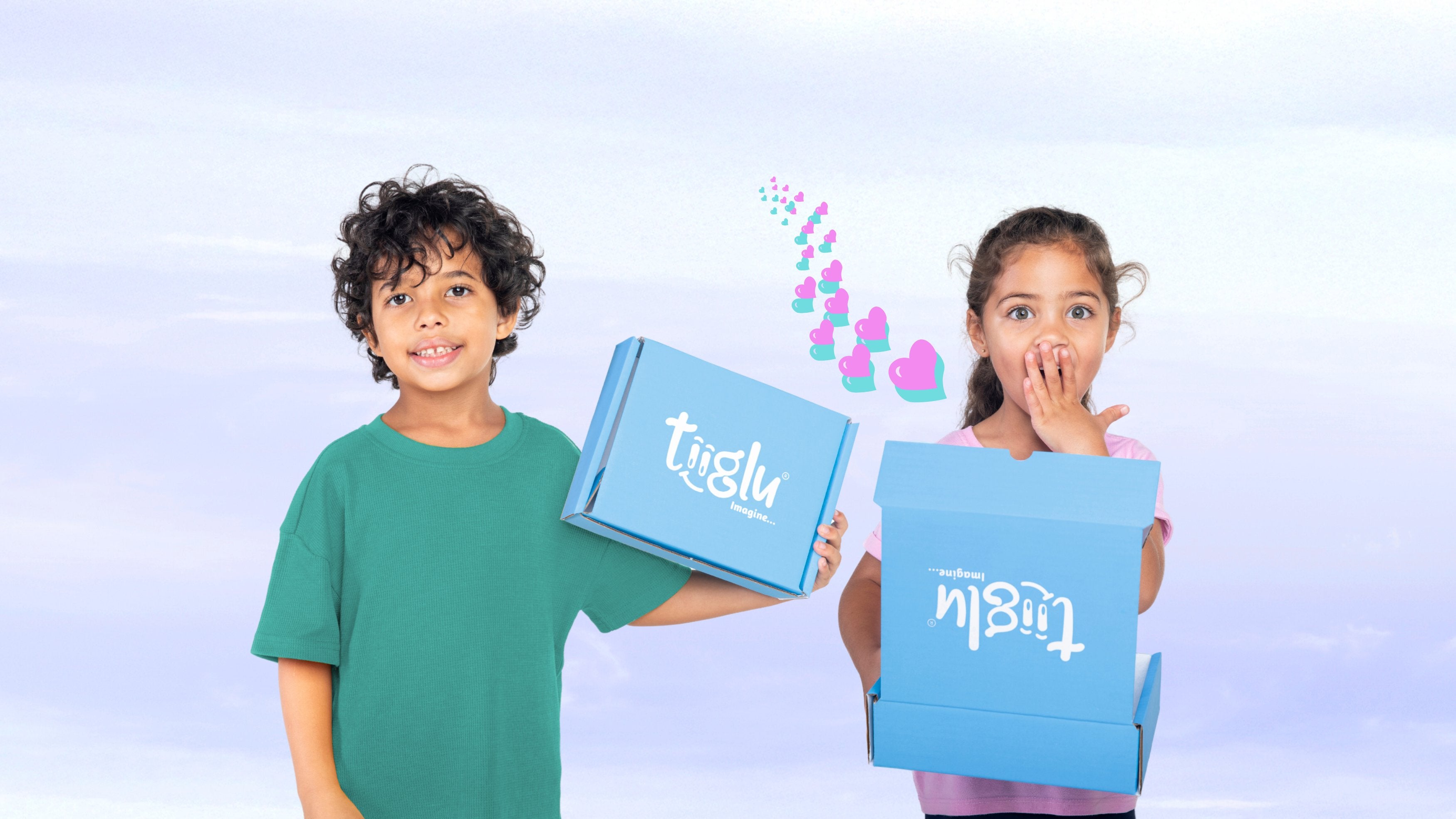 A little boy and girl hold blue Tiiglu® gift boxes on a pastel blue background with hearts. This Gifting section banner promotes e-gift cards and Dragon and Mermaid gift sets with body and hair care, plus stickers.