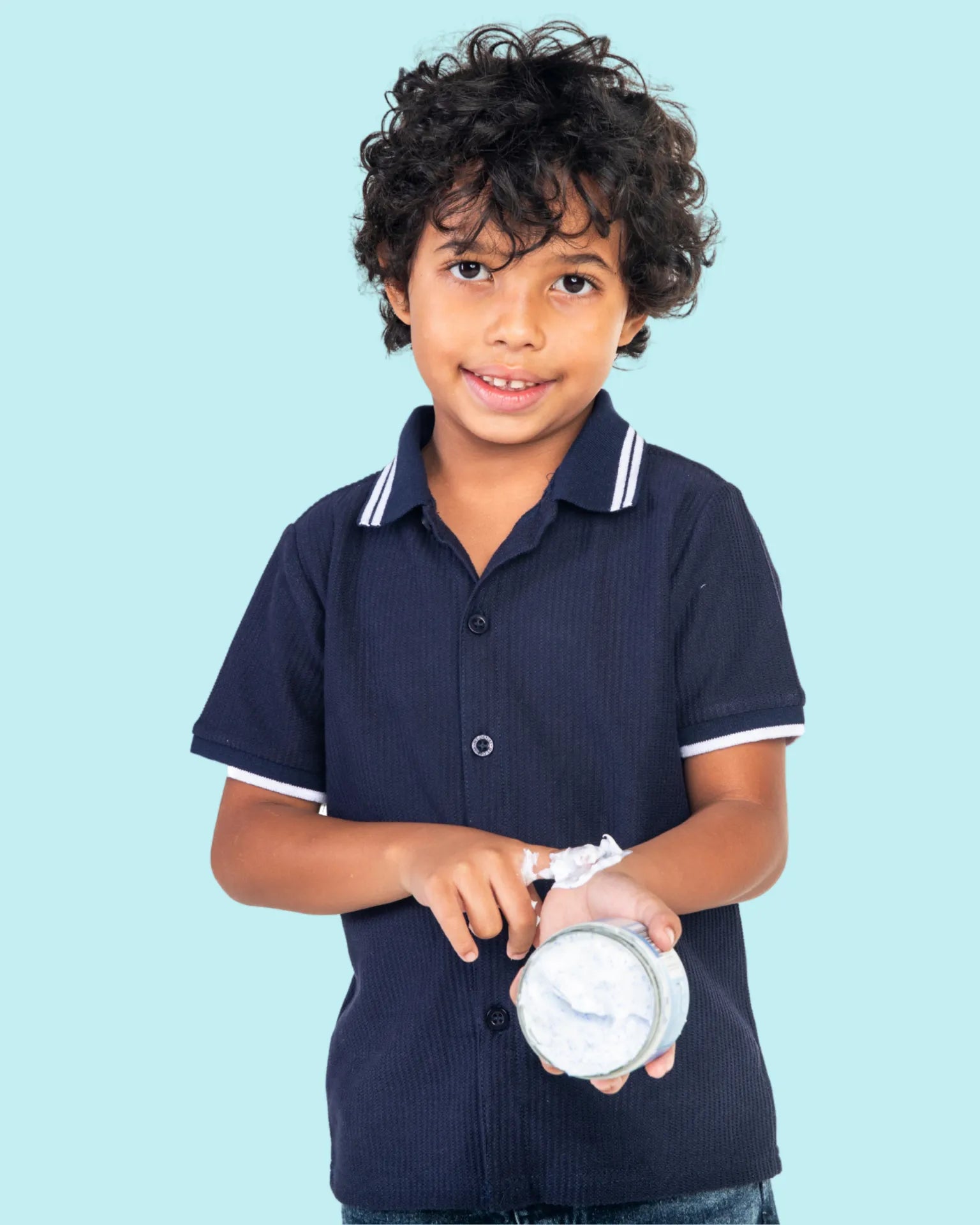 A boy in a navy shirt holds a Tiiglu® body crème container against a light blue background. This small Bath & Body section on the home page promotes bathing and moisturizing products for kids