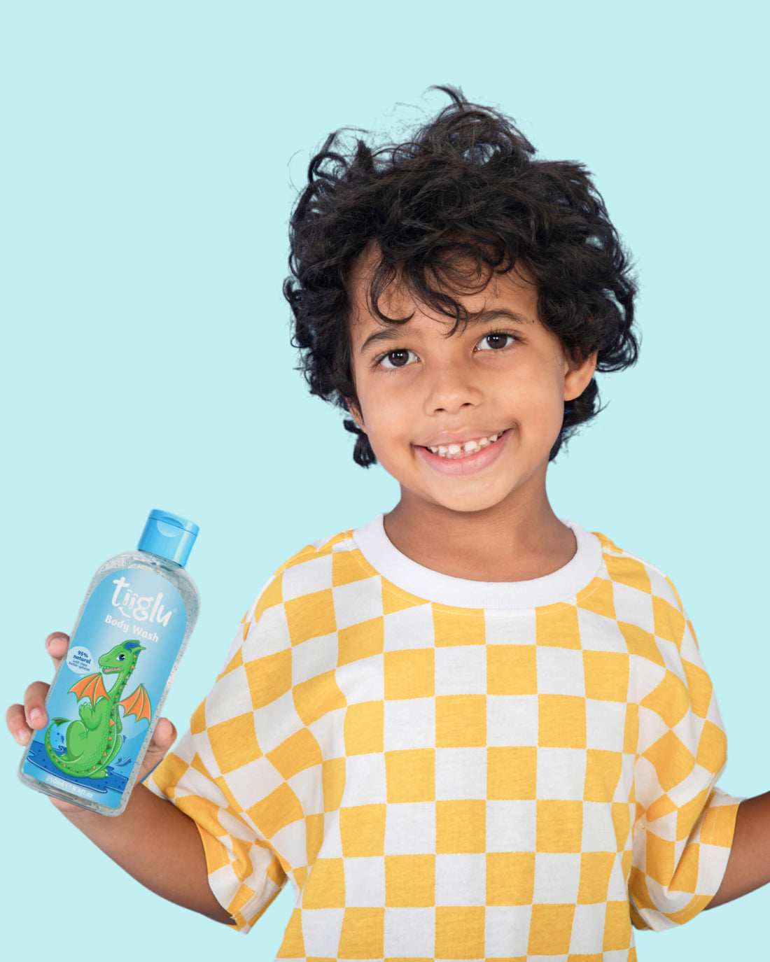 A boy in a yellow and white checkered shirt holding a Tiiglu® Kids Dragon Body Wash bottle (250ml) with a green dragon on a light blue label, &