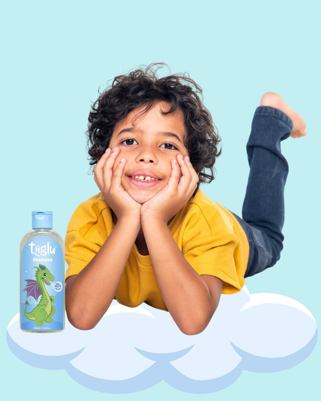 A boy in a yellow shirt lying on a cloud, holding a Tiiglu® Kids Dragon Shampoo bottle (250ml) with a green dragon on a light blue label, &